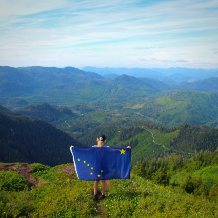 Girl standing with an Alaska flag on top of a mountain in Alaska