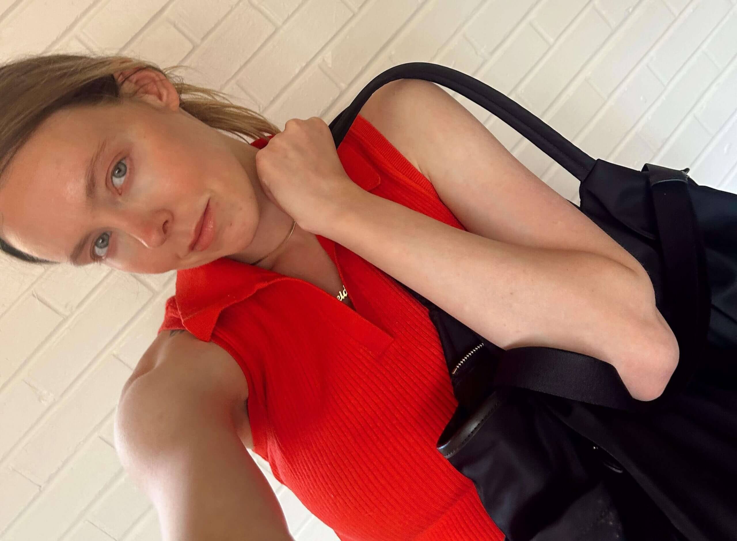 Blonde mom wearing a red shirt holding a black diaper bag